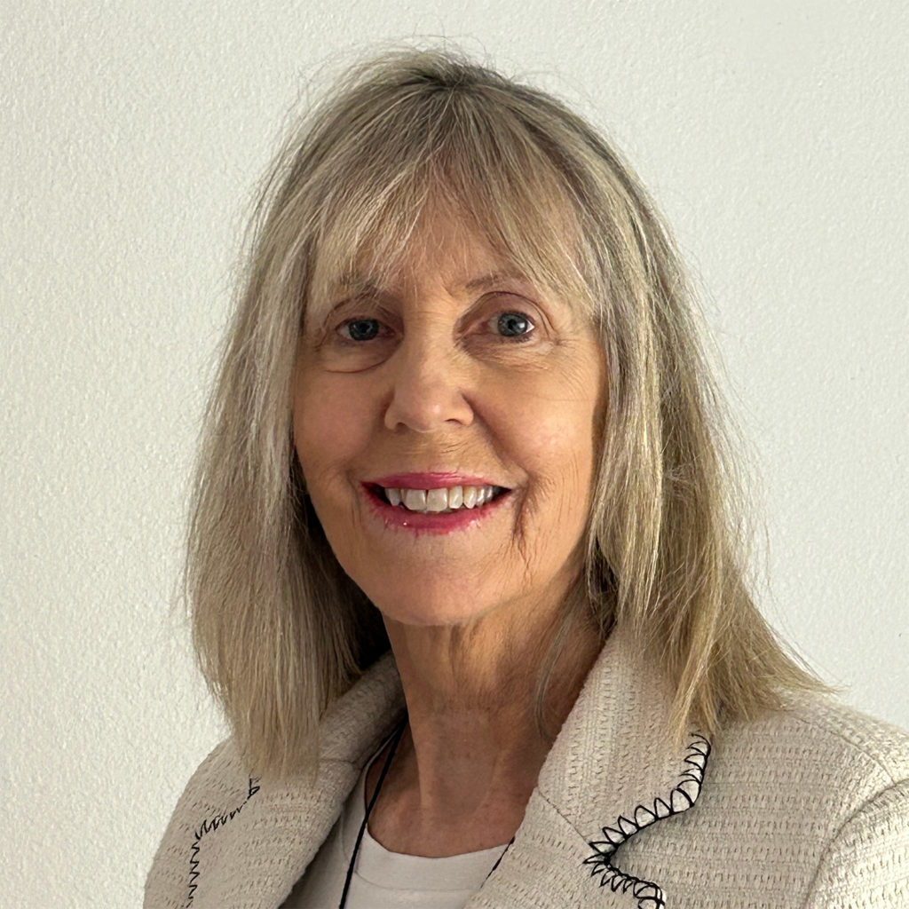 A woman with long hair wearing a white shirt, standing confidently against a neutral background.