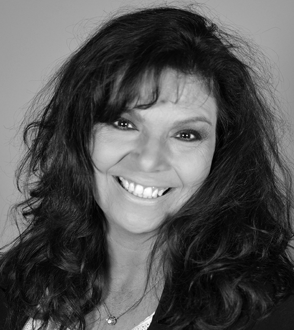 A woman with long hair smiles warmly at the camera, exuding joy and confidence.