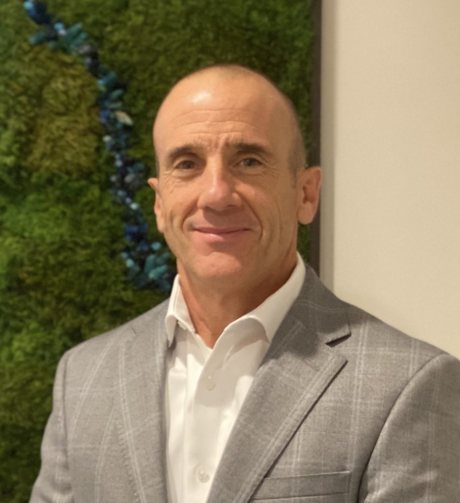 A man in a suit and tie stands confidently in front of a vibrant green wall.