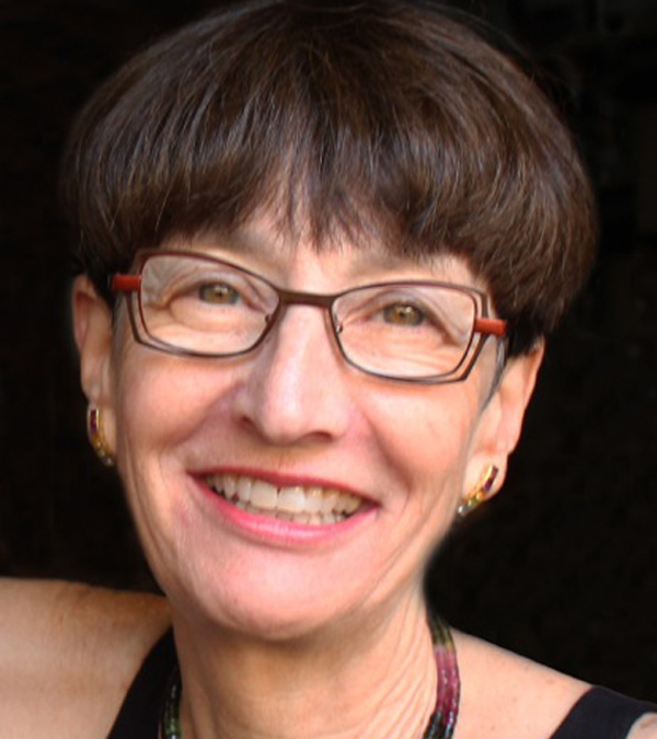 A woman wearing glasses and a necklace, smiling warmly at the camera.