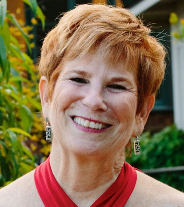 A woman with red hair smiles joyfully in front of a lush green tree, radiating warmth and happiness.